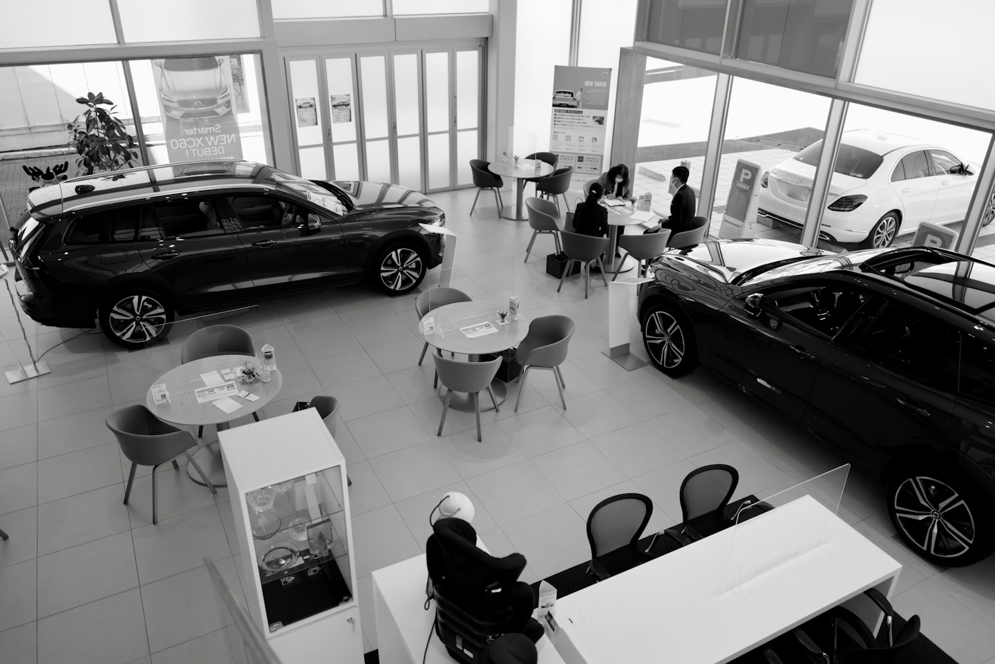 Kunden besprechen Unterlagen an Tischen in einem modernen Autohaus-Showroom.